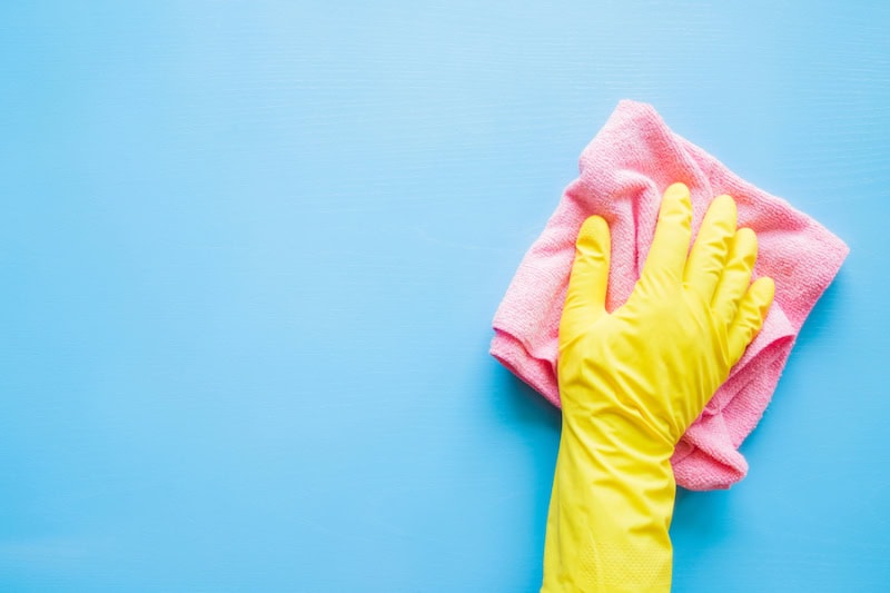 Does An AC Kill Mold? Photo of a hand in a yellow rubber glove wiping a blue wall or table with a pink cloth