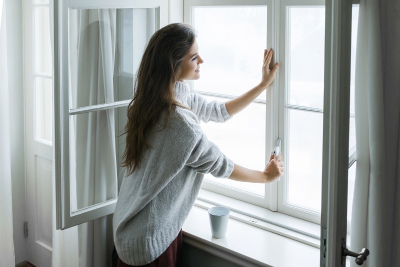 Air Handler Maintenance. Woman is opening window to look at beautiful snowy landscape outside.